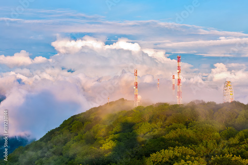 The mountain covered with a spring green forest, in which there are honeycomb towers and a Ferris wheel in huge clouds. Panorama of the Caucasian mountains from the observation tower on Mount Akhun.