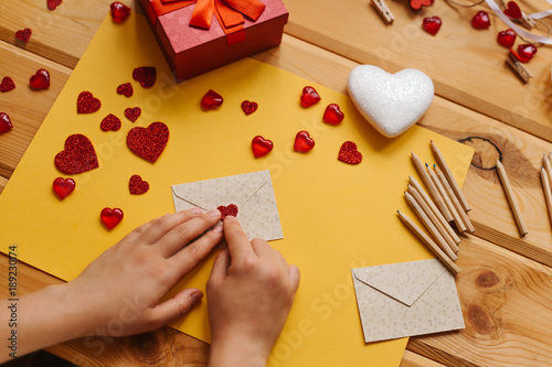 The girl wrote a letter with congratulations and pastes the envelope with a symbol in the form of a heart. Nearby lie various objects symbolizing the event.