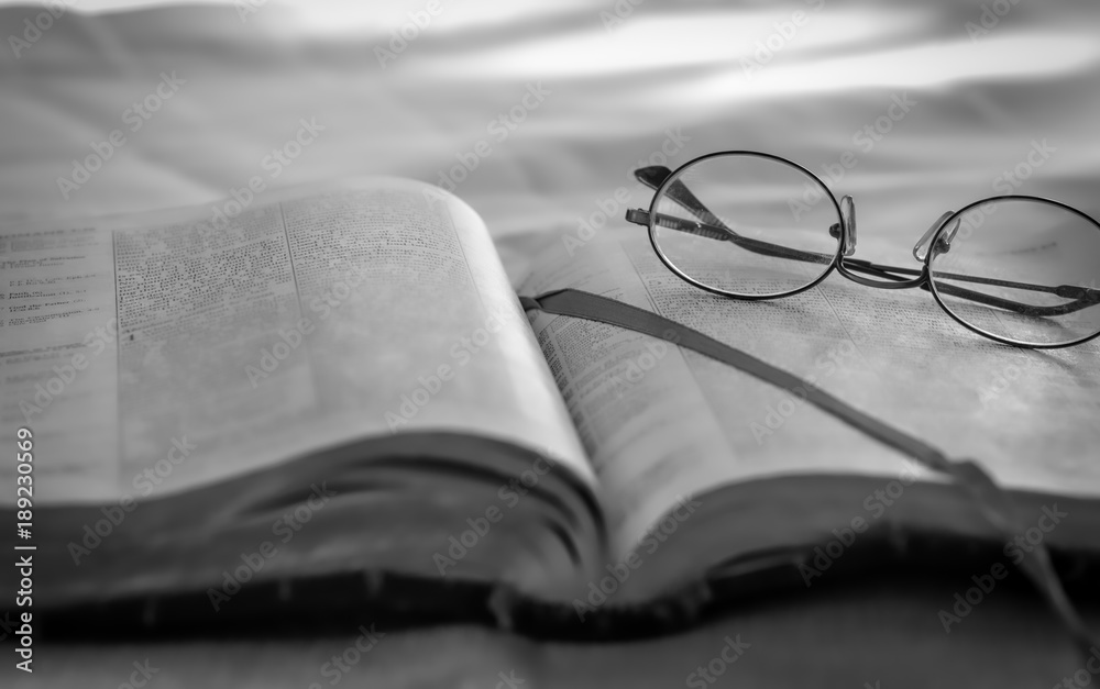 Reading old bible and glasses sitting outdoors in black and white