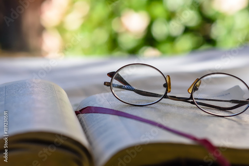 Close up glasses resting on open bible outdoors with room for text