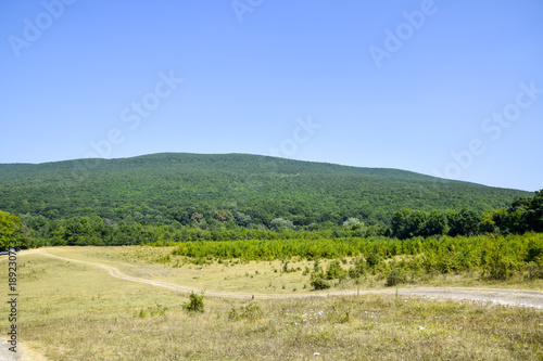 Low-mountainous landscape. A dirt road in the mountains. Forest in the hills.