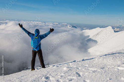 Young happy tourist on top of a snowy mountain enjoying valley view, above the clouds. Conceptual design. © sefoma