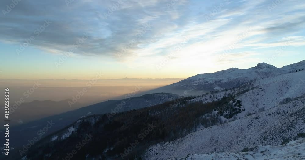 Side aerial top view over winter snowy mountain and woods forest at sunset or sunrise.Blue hour dusk or dawn twilight Alps mountains snow season establisher.4k drone flight establishing shot