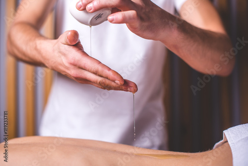 The masseur pours oil from the bowl on his hand.