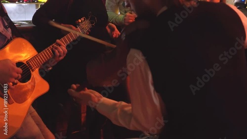 young people are celebrating in the pub. two men play the guitar and violin. live music in the bar. people are sitting on high taksoyah against the back of the bar. Holiday of drink and beer. cheerful