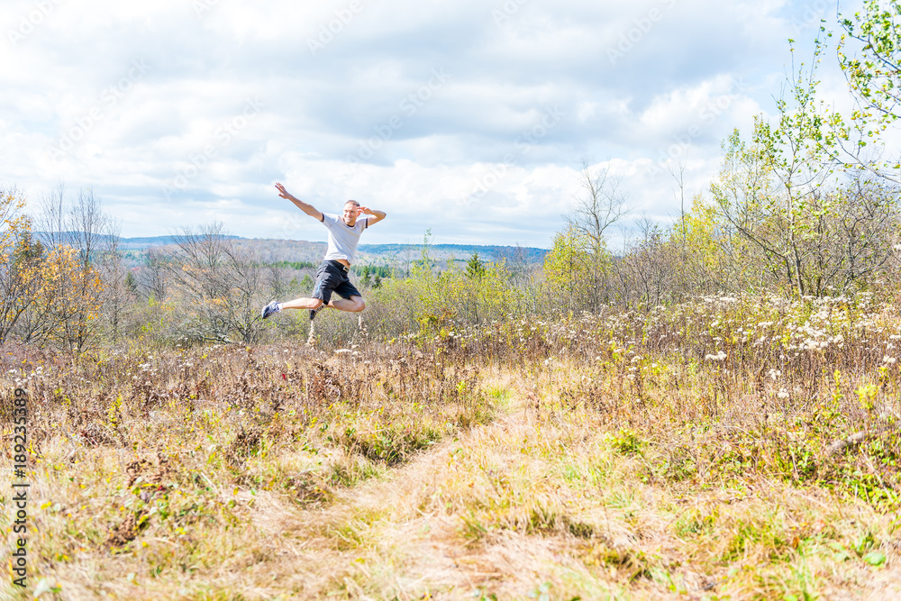 Young athletic, fit, free happy man running jogging jumping in autumn, fall, summer meadow field path hike in mid-air, muscles, front Young athletic, fit, free happy man running jogging jumping in autumn, fall, summer meadow field path hike in mid-air, muscles, front