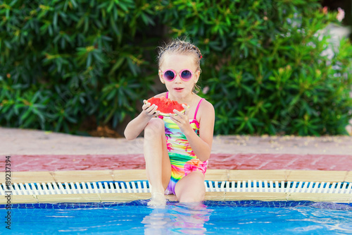 Happy girl in a swimsuit sitting by the pool with a watermelon