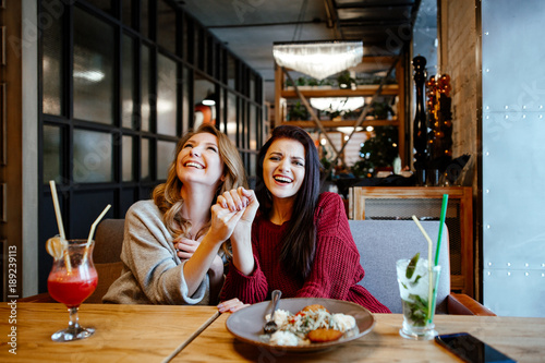 communication and friendship concept - smiling young women with nonalcoholic cocktails at cafe. two girlfriends blonde and brunette talk, joke and laugh