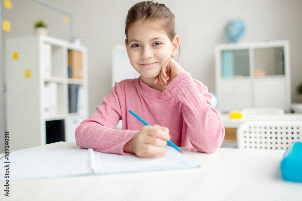 Smiling schoolgirl with crayon looking at camera while drawing at lesson Smiling schoolgirl with crayon looking at camera while drawing at lesson