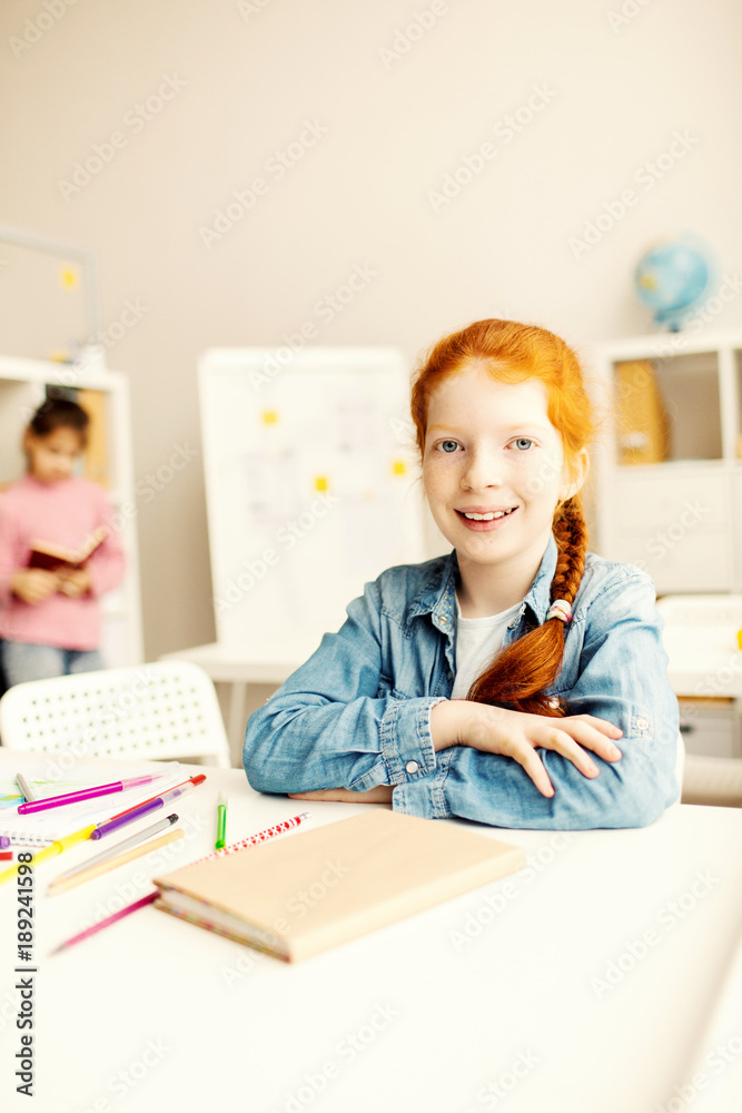 Cheerful and diligent schoolkid sitting by desk in classroom and looking at camera Cheerful and diligent schoolkid sitting by desk in classroom and looking at camera