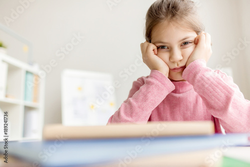 Obraz na plátne Reluctant schoolgirl touching her cheeks by hands while sitting at lesson
