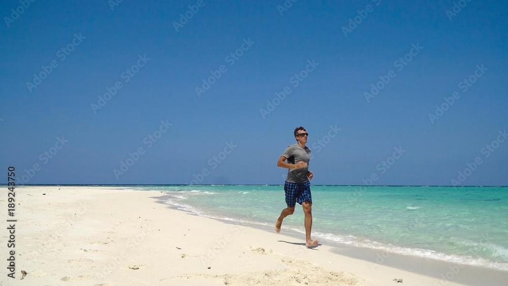Man running along beach. Fitness sports runner man jogging on beach. Handsome young fit sporty male athlete running outside on beautiful beach training. Man running along beach. Fitness sports runner man jogging on beach. Handsome young fit sporty male athlete running outside on beautiful beach training.