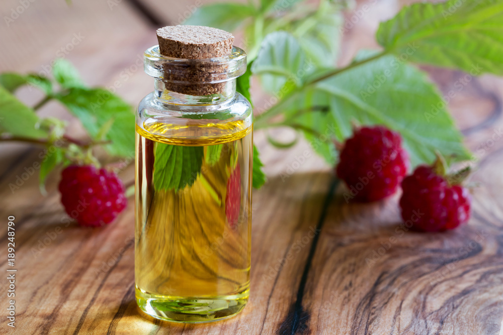 A bottle of raspberry seed oil with fresh raspberries in the background A bottle of raspberry seed oil with fresh raspberries in the background