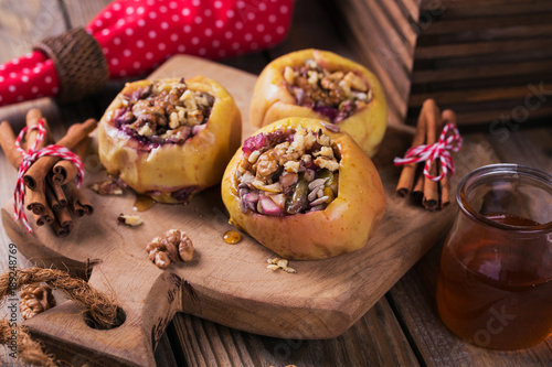 Baked apples stuffed with berries, walnuts and honey on a wooden cutting board.