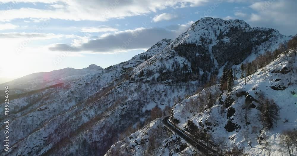 Forward aerial top view over car travelling on road in Winter snow mountain near forest woods.Snowy mountains street path establisher.Sunset or sunrise sun backlit.4k drone flight establishing shot Forward aerial top view over car travelling on road in Winter snow mountain near forest woods.Snowy mountains street path establisher.Sunset or sunrise sun backlit.4k drone flight establishing shot