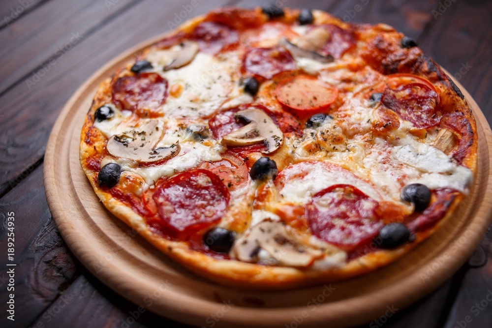 Freshly baked pepperoni pizza with mushrooms on the wooden plate, close up. Italian food