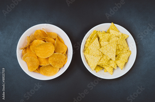 Party snacks - potato chips and snacks in bowl on black slate table. Photograph taken from above, top view with copy space around products.