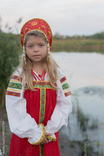 Smiling little Caucasian girl in Russian national costume outdoor with blur natural landscape background