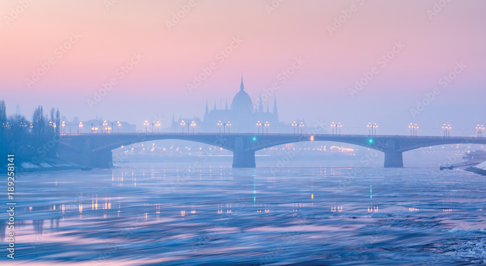 Naklejka premium Panoramic view of Margaret bridge against Parliament outline in winter haze under pink sky