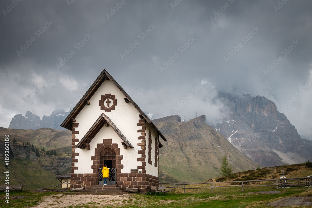 Woman in a yellow raincoat infront of chapel at Rolle Pass, Italy