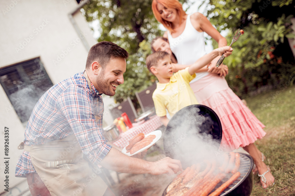 Man preparing barbecue while family having meal in the backyard.