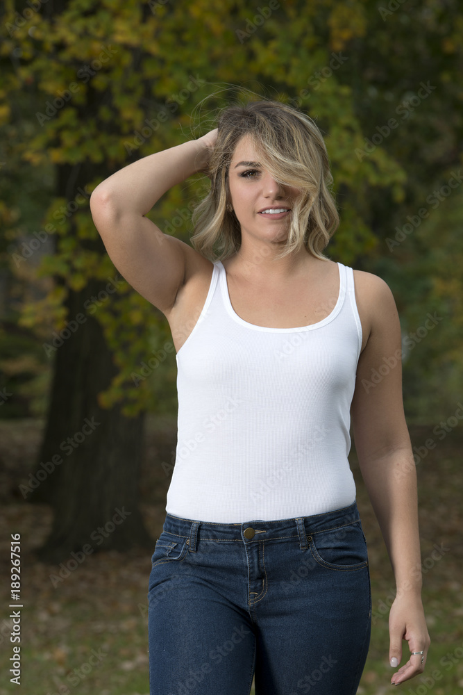Beautiful Caucasian female model poses in white tank top and blue jeans in park Beautiful Caucasian female model poses in white tank top and blue jeans in park