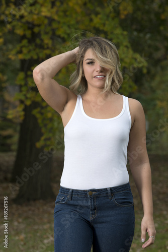 Beautiful Caucasian female model poses in white tank top and blue jeans in  park Stock Photo