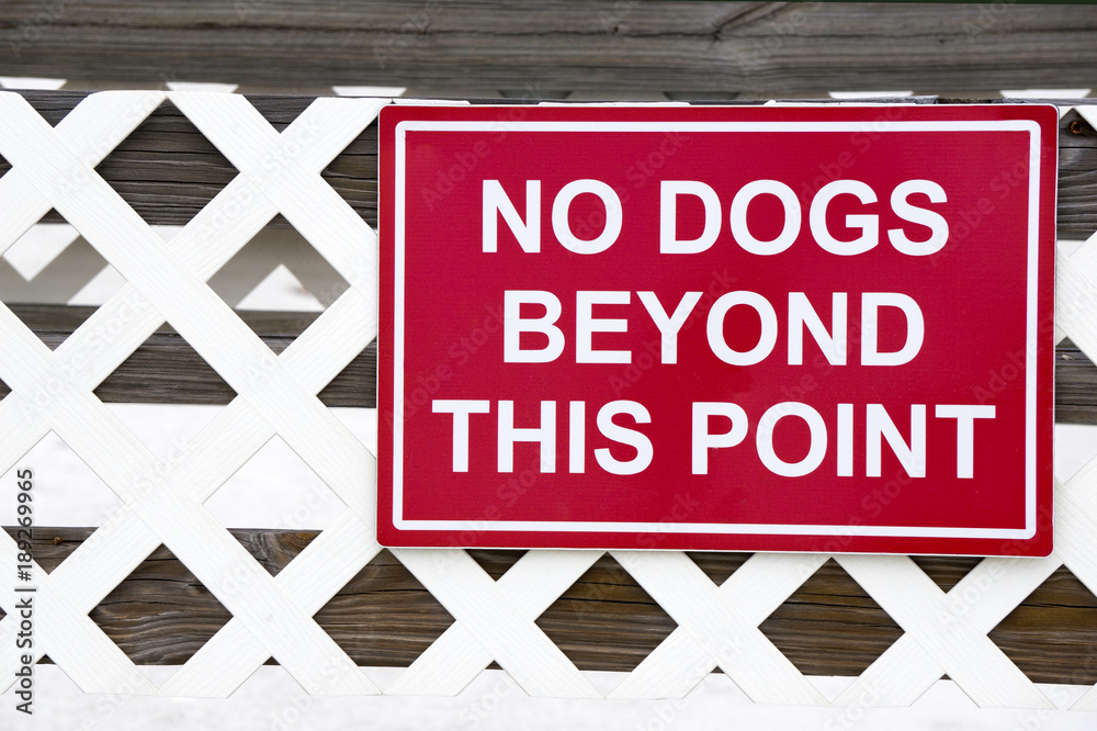 A no dogs allowed sign posted on a fence along a boardwalk on a sandy beach on the Gulf of Mexico at St. Pete Beach, Florida.