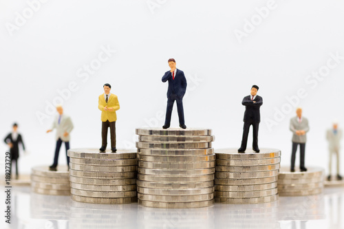 Miniature people : Businessman standing on stack of coins. Image use for difference in job position of business.