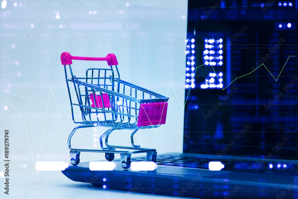 Double exposure Shopping cart trolley with laptop notebook and stock market display, e-commerce and online shopping concept.