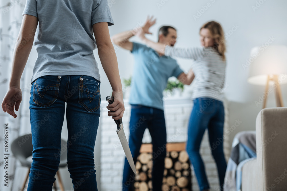 Shouting. Fearless slim young girl holding a knife and watching her parents while her father beating her mom Shouting. Fearless slim young girl holding a knife and watching her parents while her father beating her mom