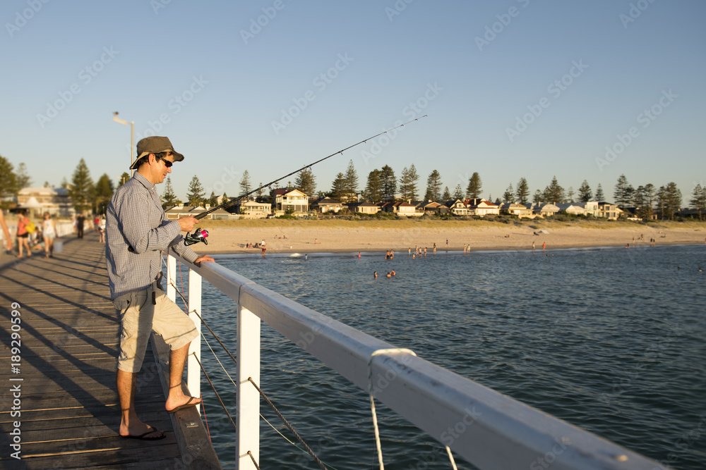 young attractive and happy man in shirt and hat fishing at beach sea dock using fish road enjoying weekend hobby in holidays