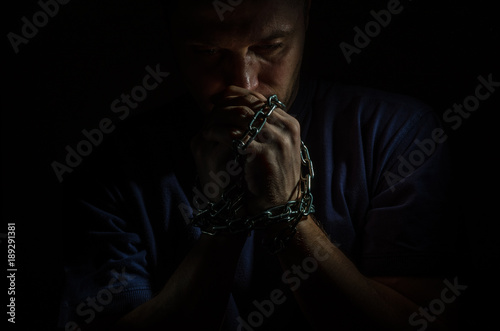 Repented man prisoner with his hands shackled in chains on a dark background Fototapet