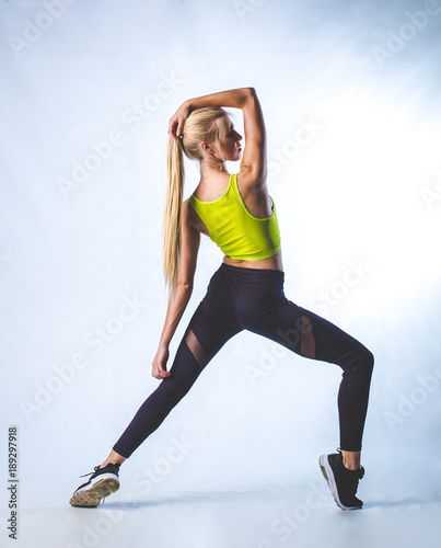 Beautiful female fitness model doing stretches and dancing in a studio, isolated against white background