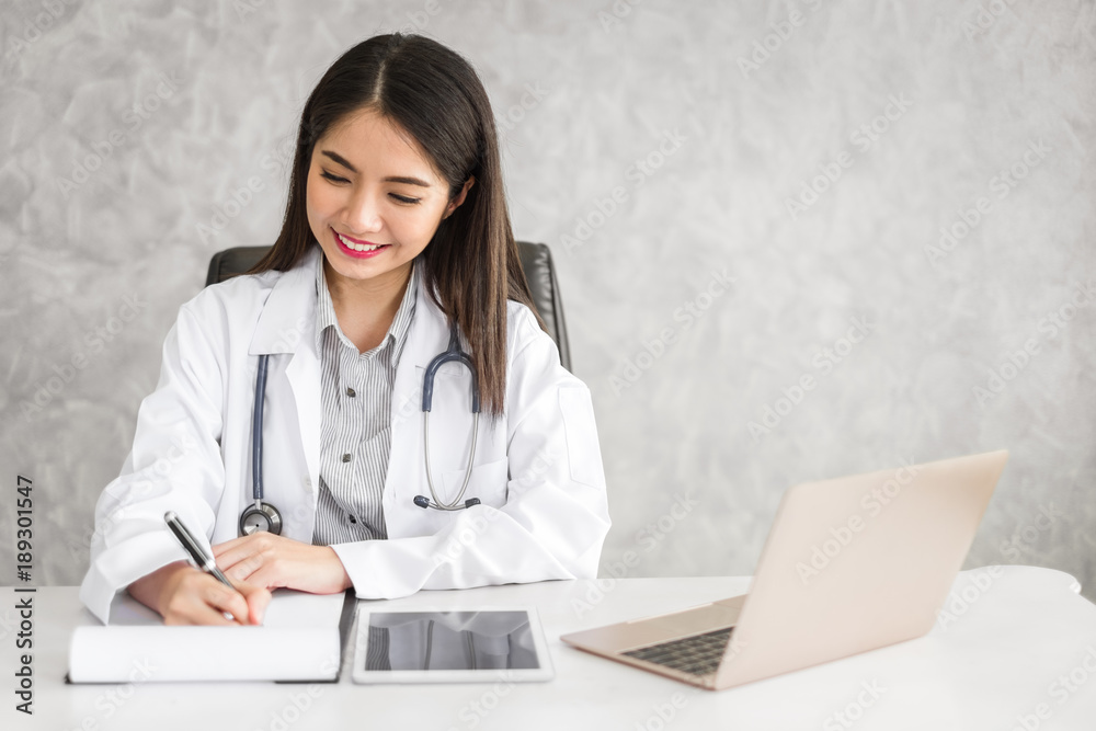 Young beautiful asian doctor woman working happy and smile in hospital, sitting on table, asian medical concept Young beautiful asian doctor woman working happy and smile in hospital, sitting on table, asian medical concept