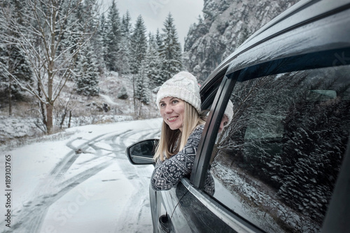 Woman at winter time. Female looking in window of her black car. 