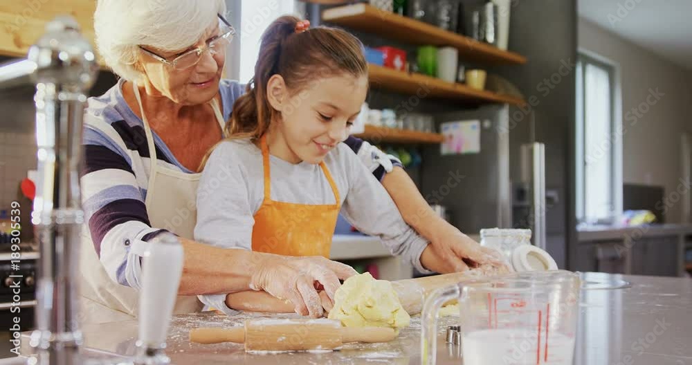 Grandmother and little girl in apron flattening dough with rolling pin  