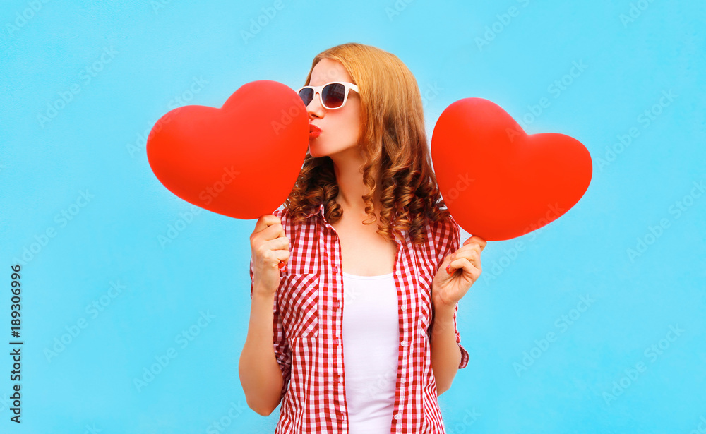 pretty woman kisses a red air balloon in the shape of a heart on blue background pretty woman kisses a red air balloon in the shape of a heart on blue background