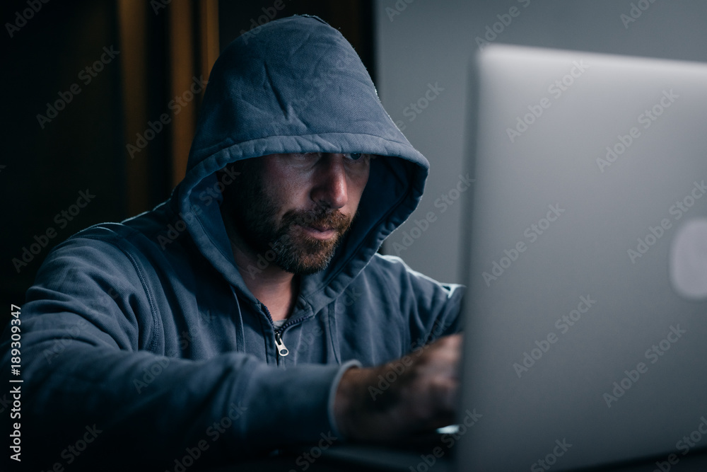 a man hacker sits in a room behind a laptop and prints something a man hacker sits in a room behind a laptop and prints something