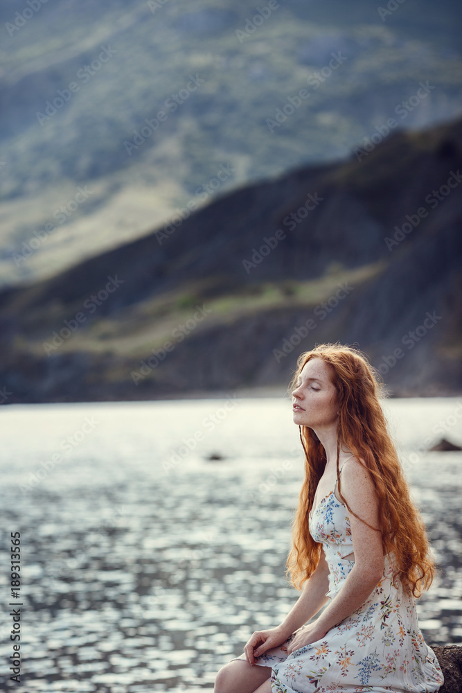 Young red-haired girl in the style of Boho. Enjoys the beauty of the sea coast. The idea and concept of freedom and hippies