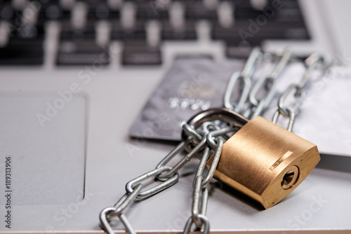 Heavy chain with a padlock around a laptop and credit card on table.