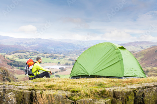 Man explorer with a tent at top of mountain