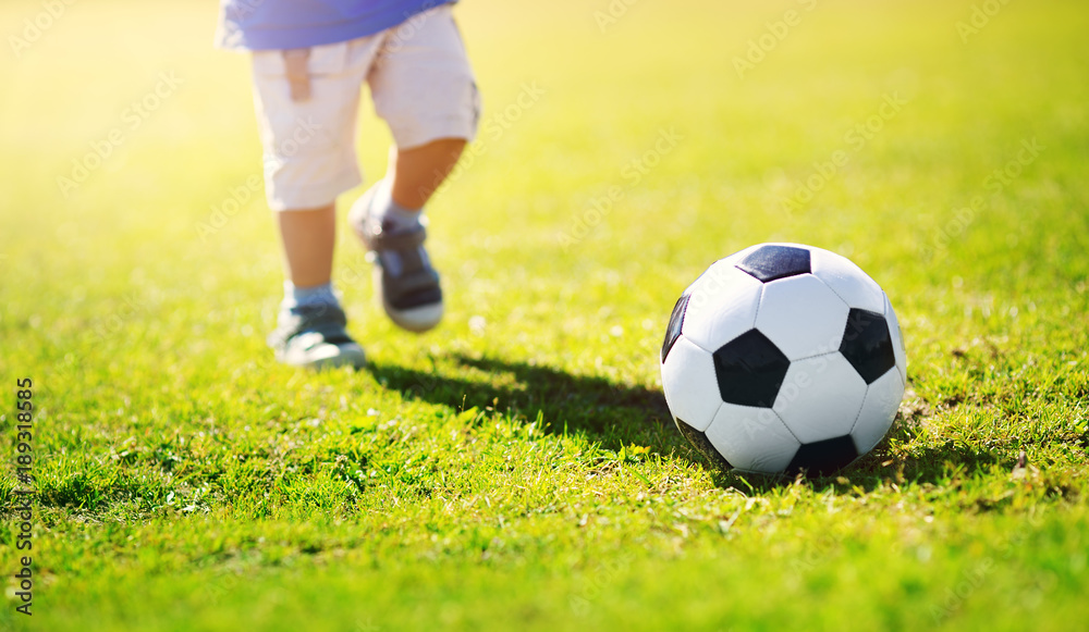 Little boy playing football on the field with gates