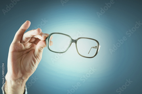 Transparent glasses in hand on empty blue background