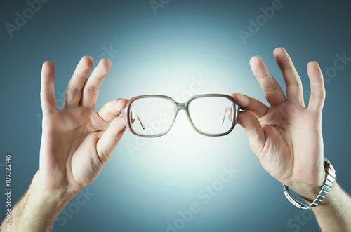 Transparent glasses in hand on empty blue background