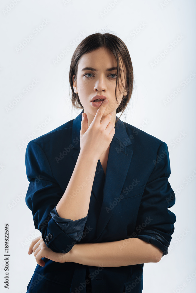Thinking process. Musing young elegant woman touching her lips and looking straight while dressing in jacket Thinking process. Musing young elegant woman touching her lips and looking straight while dressing in jacket