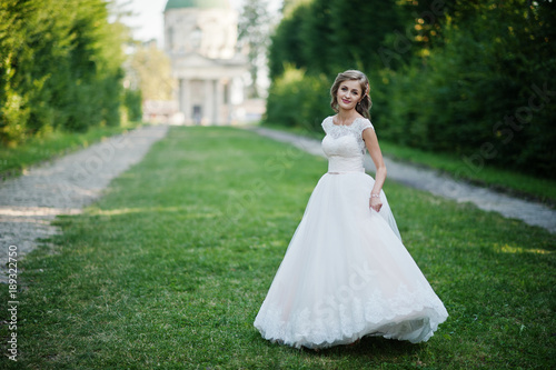 Lonely attractive bride walking on the green alley which leads to a church.