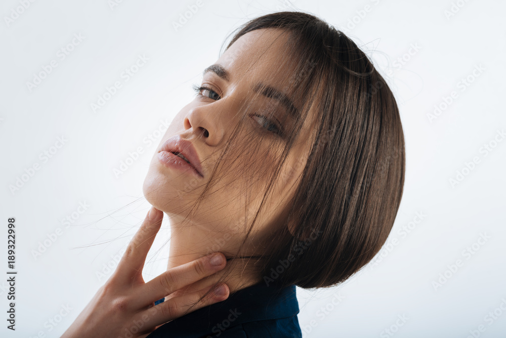 Innocent look. Sweet good looking tranquil woman gazing at the camera and posing on the isolated background while caressing her neck Innocent look. Sweet good looking tranquil woman gazing at the camera and posing on the isolated background while caressing her neck