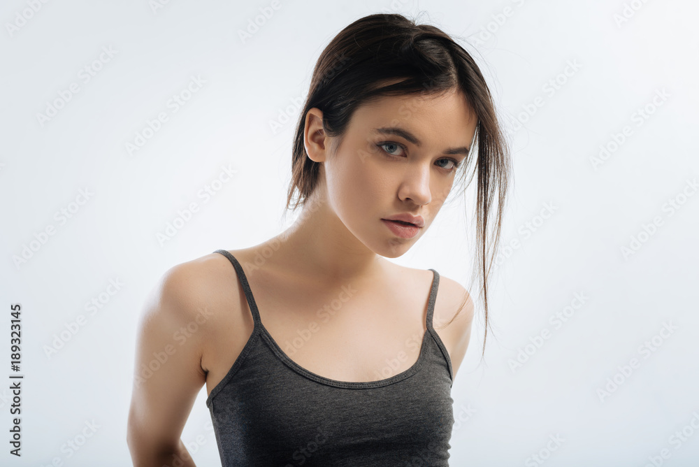 Unbelievable news. Focused attractive confident woman gazing at the camera and standing on the light background and listening to news