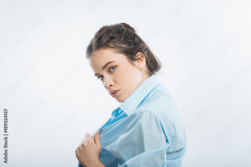 Woman power. Irresistible pleasant young woman looking at the camera and posing on the isolated background while playing with shirt Woman power. Irresistible pleasant young woman looking at the camera and posing on the isolated background while playing with shirt